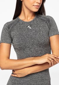 Hallgray lühikeste varrukatega spordiülikond, millel on voolujooneline disain, tekstuuriga kangas ja valge logo kaeluses. Ülikond paistab silma sujuvate joonte ja varrukatega.