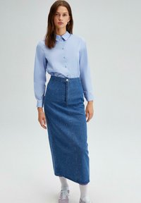 Chemise boutonnée à manches longues bleu clair associ�ée à une jupe en denim taille haute ornée de perles et avec une fermeture à boutons sur le devant.