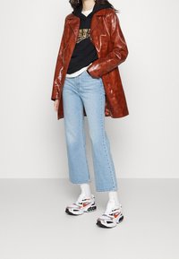 Gabardina de cuero marrón, sudadera negra con capucha, jeans acampanados de color azul claro y zapatillas blancas con acentos rojos y negros. Textura suave, diseño contemporáneo.
