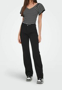 Mustat korkeavyötäröiset housut yhdistetty mustavalkoiseen raidalliseen ribbipaitaan, jossa on puffihihat. Asu viimeistellään mustilla lenkkareilla.