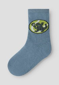 Μπλε βαμβακερή κάλτσα με γραφικό μαύρης γάτας που κρατάει ένα ρακέτα τένις, σε πράσινο οβάλ φόντο. Κουβάρια με υφή.