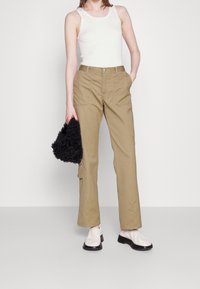 Khaki cargo-housut slim fit -mallissa, joissa on sivutaskut, yhdistettynä ribattuun valkoiseen tank topiin ja mustaan teksturoituun käsilaukkuun. Valkoiset nilkkurit täydentävät asun.