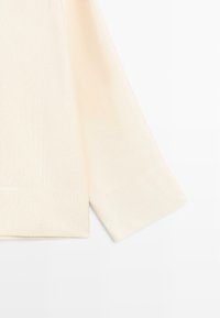 Lichtbeige trui met een zachte textuur, voorzien van een brede, comfortabele mouw en een rechte zoom, gemaakt van een geribbelde breistof.