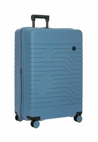 Valigia rigida blu chiaro con motivo a onde testurizzato, manico nero e quattro ruote per la mobilità. Chiusura con cerniera sulla parte frontale.