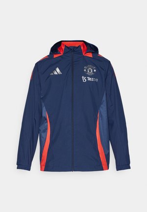 Giacca a vento navy con accenti rossi, zip frontale, cappuccio e dettagli del logo. Realizzata in tessuto leggero con una texture liscia.