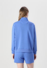 Hemelsblauwe sweatshirt met hoge kraag en geribbelde manchetten, gecombineerd met bijpassende shorts. Zachte stof, casual ontwerp en minimalistische details.