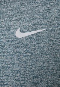 Vitt Nike Swoosh-logotyp på texturerad blå och grå sporttygsbakgrund.
