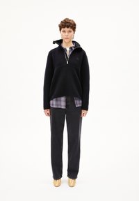 Pullover in pile blu navy con zip a metà, indossato sopra una camicia a quadri. Abbinato a jeans neri a gamba larga e scarpe gialle lucide.