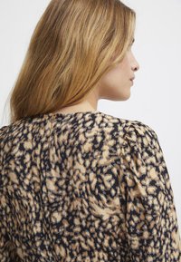 Langærmet bluse med leopardprint i beige og sort, rund halsudskæring og subtile plisseringer ved skuldersømmene.