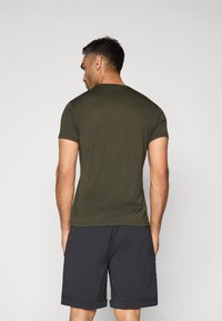 Olivengrønn kortermet t-skjorte med rund hals, brukt sammen med mørkegrå shorts. Tettsittende design, jevn tekstur og minimalt med detaljer.