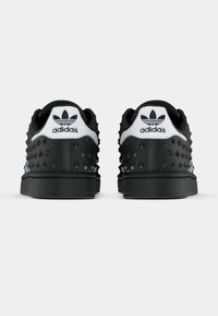 Baskets noires en caoutchouc texturé, avec une languette de talon blanche, un logo en relief et des points en relief sur les côtés.