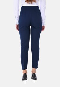 Pantaloni navy su misura, forma aderente, texture liscia, con gambe slim e vita alta. Indossati con scarpe nere con tacco alto.