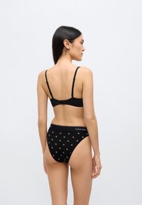 Μαύρο σουτιέν με ρυθμιζόμενες τιράντες και κλείσιμο με κόπιτσα, συνδυασμένο με μαύρο ψηλόμεσο εσώρουχο που διαθέτει επαναλαμβανόμενο μοτίβο με το λογότυπο CK.