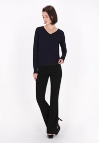 Maglione a V navy abbinato a pantaloni neri svasati e tacchi neri. Tessuto morbido con un design aderente, accenti minimi e silhouette elegante.