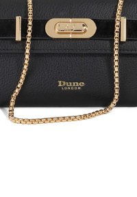 Black leather handbag with a gold chain strap, featuring a gold clasp and a patent leather accent. "Dune London" is embossed on the front.