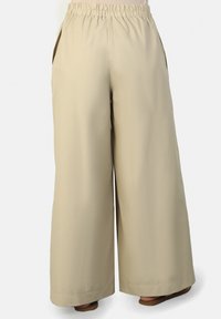 Beige wide-leg pants with an elastic waistband, side pockets, and smooth fabric, featuring a floor-length cut and clean hemline.