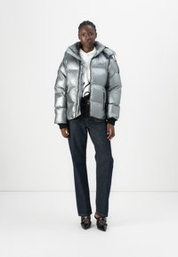Giacca a vento argento con cappuccio, caratterizzata da una texture lucida e un design trapuntato. Abbinata a jeans in denim scuro e scarpe nere a punta.