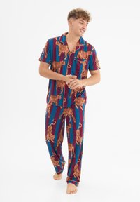 Pyjaman set dengan atasan lengan pendek dan celana panjang, menampilkan pola garis-garis biru dan burgundy dengan ilustrasi harimau oranye. Bahan katun.
