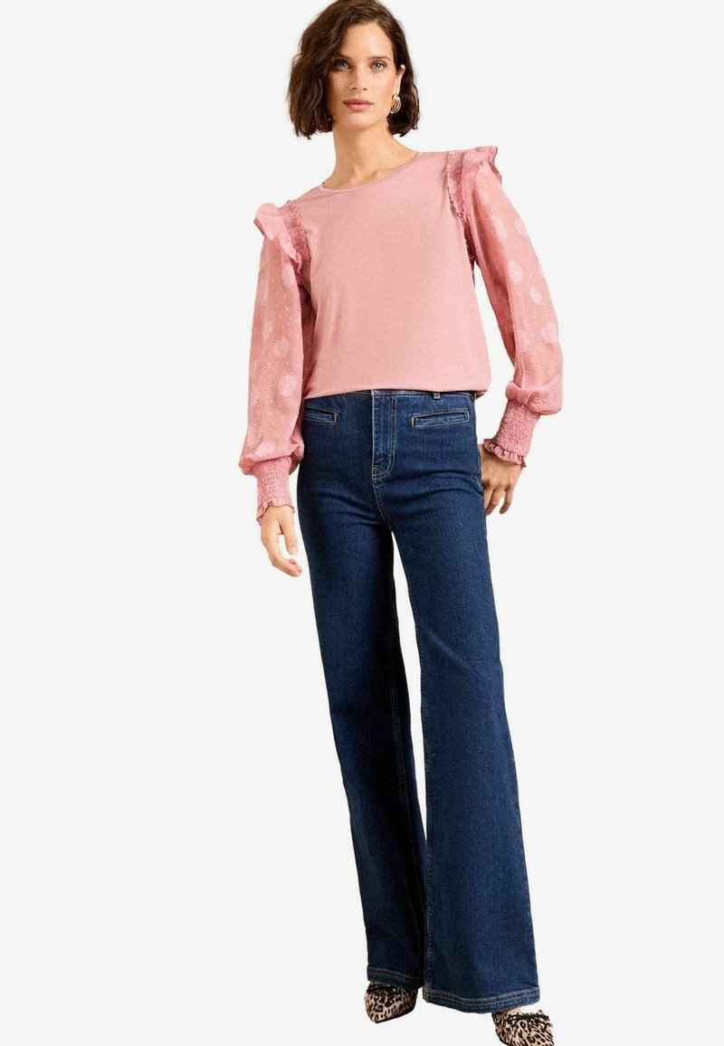 Top rosa chiaro con maniche a sbuffo, motivo a pois, abbinato a jeans a zampa d'elefante blu scuro. Maniche strutturate e dettaglio dell'orlo aderente.
