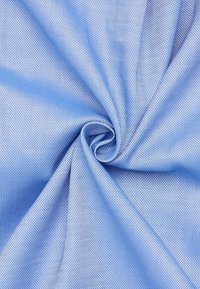 Tissu bleu clair avec un tissage texturé, présentant une surface lisse et un aspect doux, légèrement brillant, disposé en forme de spirale.