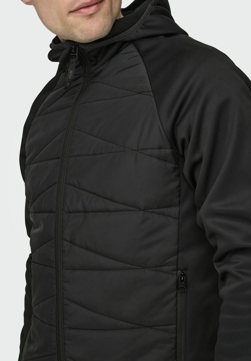 Veste isolante noire avec un motif matelassé, dotée d'une fermeture éclair sur le devant, d'une capuche et de panneaux en tissu lisse sur les manches et les côtés.