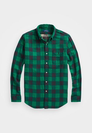 Chemise à manches longues à carreaux verts et noirs avec poche poitrine et col, étalée à plat sur un fond blanc.