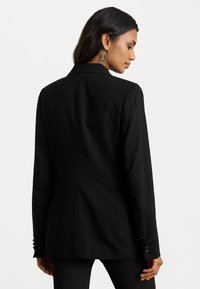 Melnas pielāgotas žaketes ar strukturētu dizainu, teksturētu audumu, cietu aizmuguri un pogu dekorācijām uz piedurknēm.