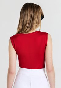 Top corto senza maniche rosso con una texture liscia, scollatura rotonda e cuciture pulite, abbinato a pantaloni bianchi a vita alta.