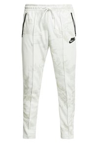 Vita atletiska byxor med ett subtilt bladmönster, elastisk midja, dragsko och svarta dragkedjefickor på sidorna. Nike-logga applicerad.