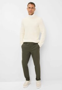 Off-white struktureret strikket turtleneck sweater parret med mørkegrønne bukser og beige sneakers, som har en slank pasform og et minimalistisk design.