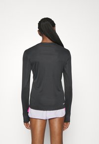 Pitkähihainen musta urheilupaita, jossa on sileä pinta. Ominaisuuksiin kuuluu pyöreä kaula-aukko ja tiukka malli, yhdistettynä vaaleanpuniin lyhyisiin housuihin, joissa on vaaleanpunaisia yksityiskohtia.