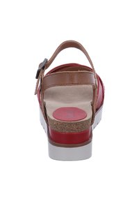 Red sandal with a cork footbed, brown leather strap, adjustable buckle, and a white outsole. Smooth texture with a circular design on the footbed.