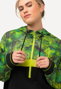 Giacca con cappuccio verde e nera con zip frontale, caratterizzata da una vistosa striscia gialla, motivi testurizzati e cordini regolabili.
