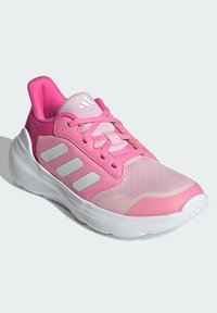 Różowy but sportowy z siateczkową cholewką, trzema białymi paskami, okrągłym noskiem, wyściółką przy języku, teksturowanym sznurowadłem i białą gumową podeszwą.