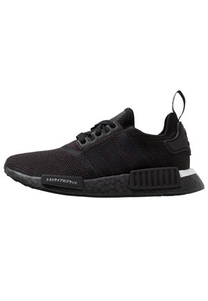 Sort Adidas sneaker med strikstof, tre striber på siden, sort sål med teksturerede blokke og trækstrop ved hælen.