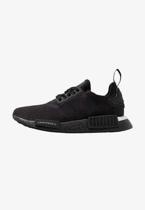 Zapatilla negra Adidas con tejido de punto, tres rayas en el lateral, suela negra con bloques texturizados y cinta para tirar en el talón.