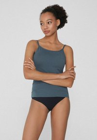 Tmavě tyrkysový, bezramínkový top s kulatým výstřihem a tenkými popruhy, doplněný černými bikiny. Hladký povrch, neformální design.