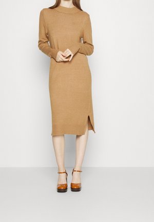 Abito a maglia color beige con maniche lunghe, colletto alto, dettagli a coste e uno spacco laterale. Indossato con tacchi a piattaforma arancioni lucidi.