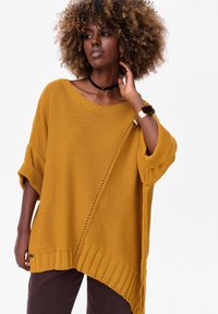 Mosterdgele oversized gebreide trui met een brede hals, geribbelde zoom en gedetailleerde stiksels, met grote mouwen en een zijaccent.