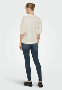 Cream-colored sweatshirt with puff sleeves, paired with dark blue skinny jeans and black platform shoes. Back view shows ribbed cuffs.