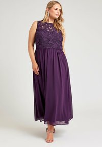 Pitkä violetti mekko, jossa on pitsipainatus, hihaton muotoilu ja kelluva halkio. Ominaisuuksiin kuuluu pyöreä pääntie ja hienovarainen läpinäkyvyys helman kohdalla.