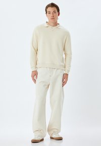 Crème-kleurige sweatshirt met een kraag, gecombineerd met brede crème broek. Gelaagd stof, losse pasvorm, minimale stikdetails.