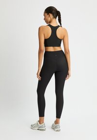 Conjunto atlético negro que incluye una camiseta ajustada con diseño de espalda nadadora y leggins de cintura alta a juego, combinados con zapatillas grises.
