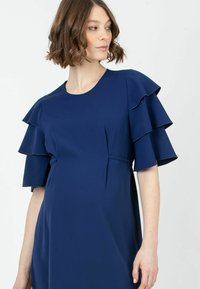 Laivansinis mekko, jossa on lyhyet röyhelöhihoja, pyöreä pääntie ja hyvin istuva vyötärö, valmistettu sileästä kankaasta, jossa on mattapinta.