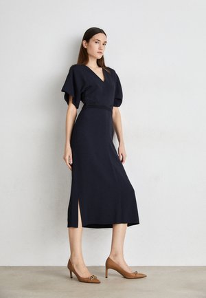 Navy blue, knee-length dress with a V-neck, short puff sleeves, and a side slit. Paired with tan high-heeled pumps featuring decorative accents.