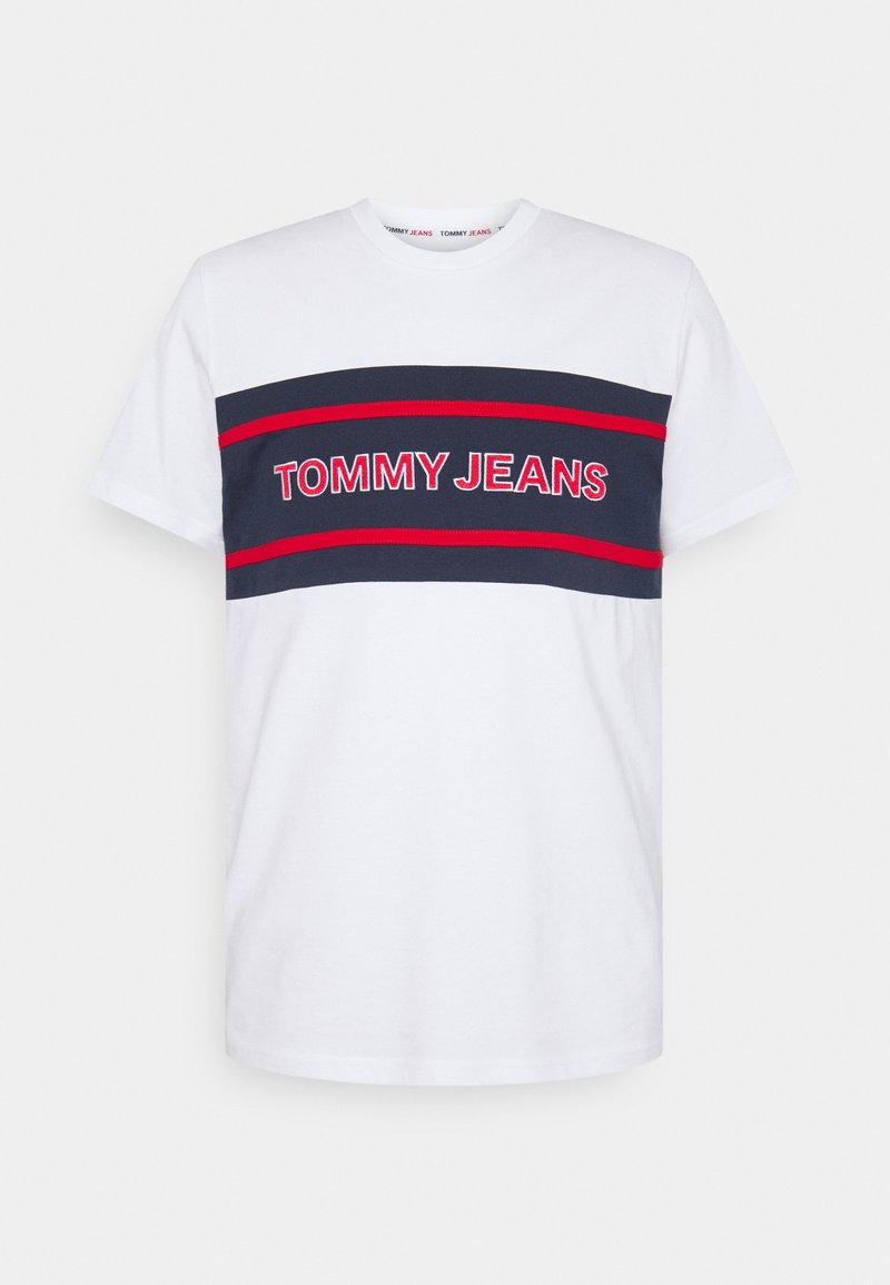 Vit bomulls-T-shirt med marinblå horisontella ränder. Har texten "TOMMY JEANS" i röd skrift över bröstet. Kort ärm, rundad halsringning.