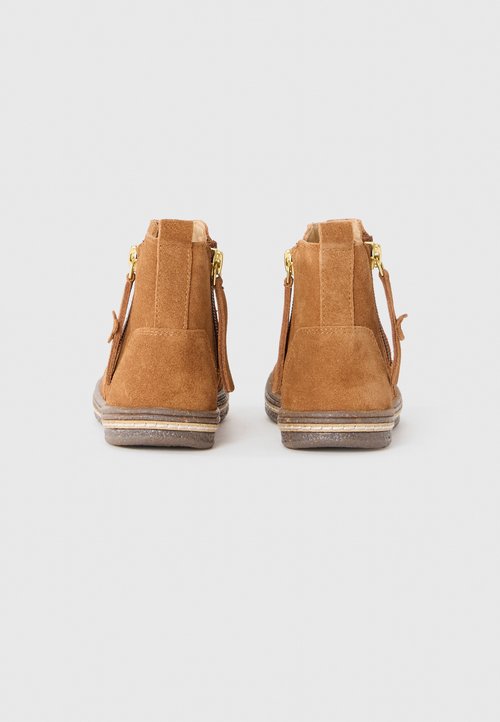 Bruine suède enkellaarsjes met een ritssluiting aan de zijkant, gouden accenten en een getextureerde rubberen zool. Kenmerken zijn onder andere een iets verhoogde hak en een ronde neus.