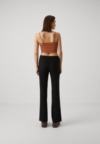 Cropped orange top with wavy pattern, thin straps; paired with black flared pants. The outfit has a smooth texture and minimal detailing.