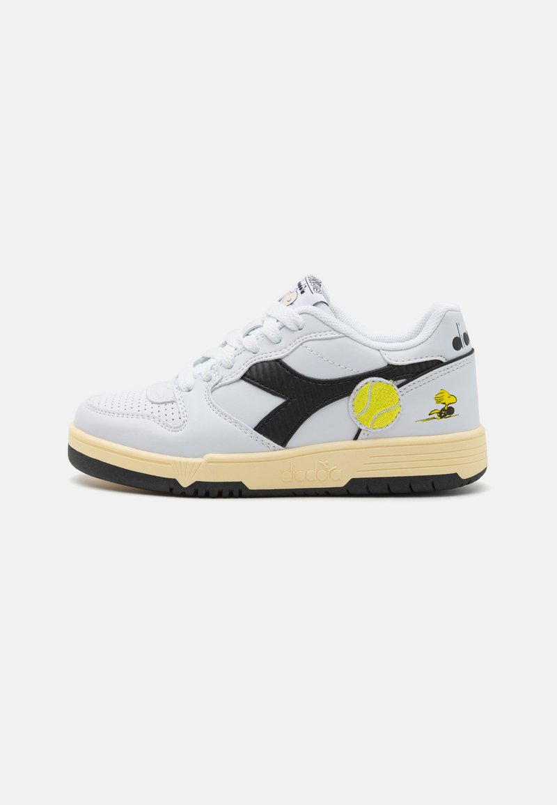 Hvit lær sneakers med svarte aksenter, teksturert overflate, gul tennisball broderi og gummisåle med en kontrasterende beige mellomsåle.