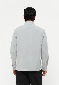 Gray corduroy shirt with vertical stripes, long sleeves, button cuffs, and a collared neckline. Features a straight hem and back yoke.